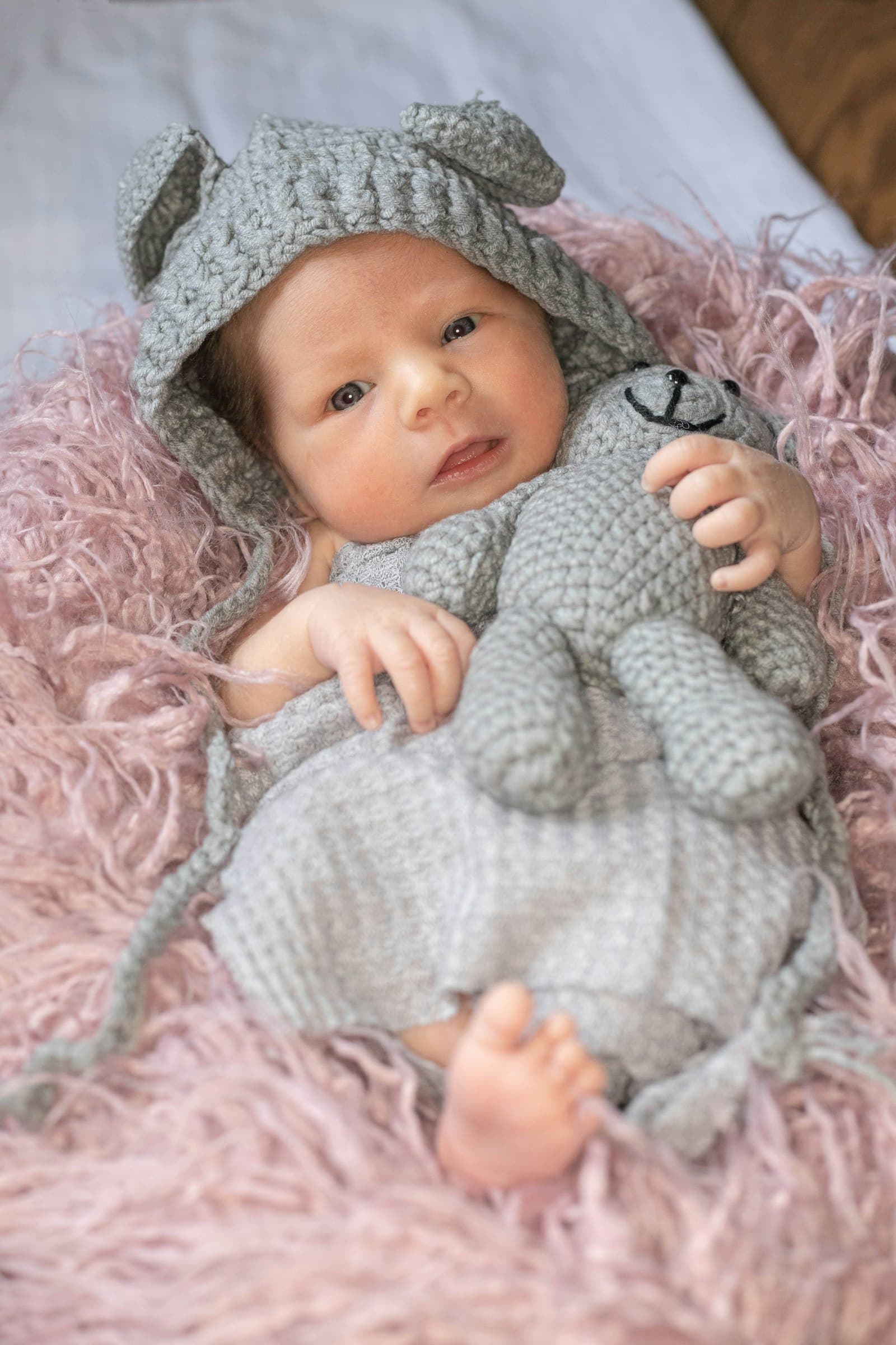 Baby in white knit sweater lying on pink textile