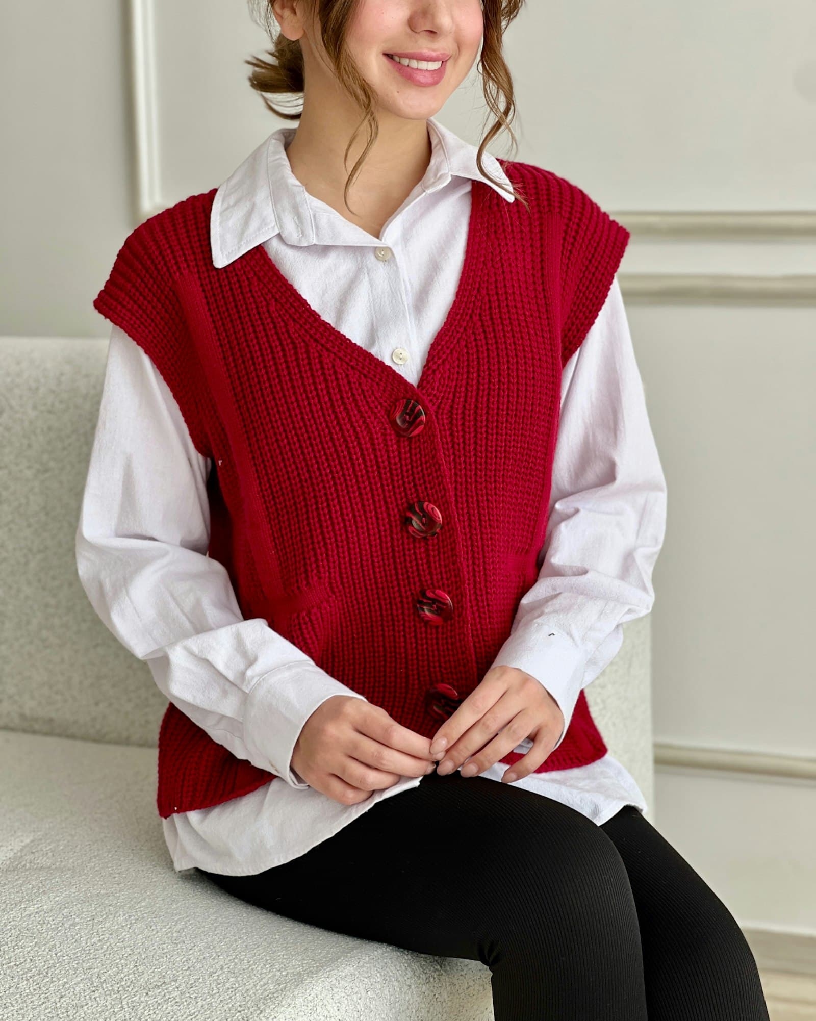 A woman sitting on a white couch wearing a red vest