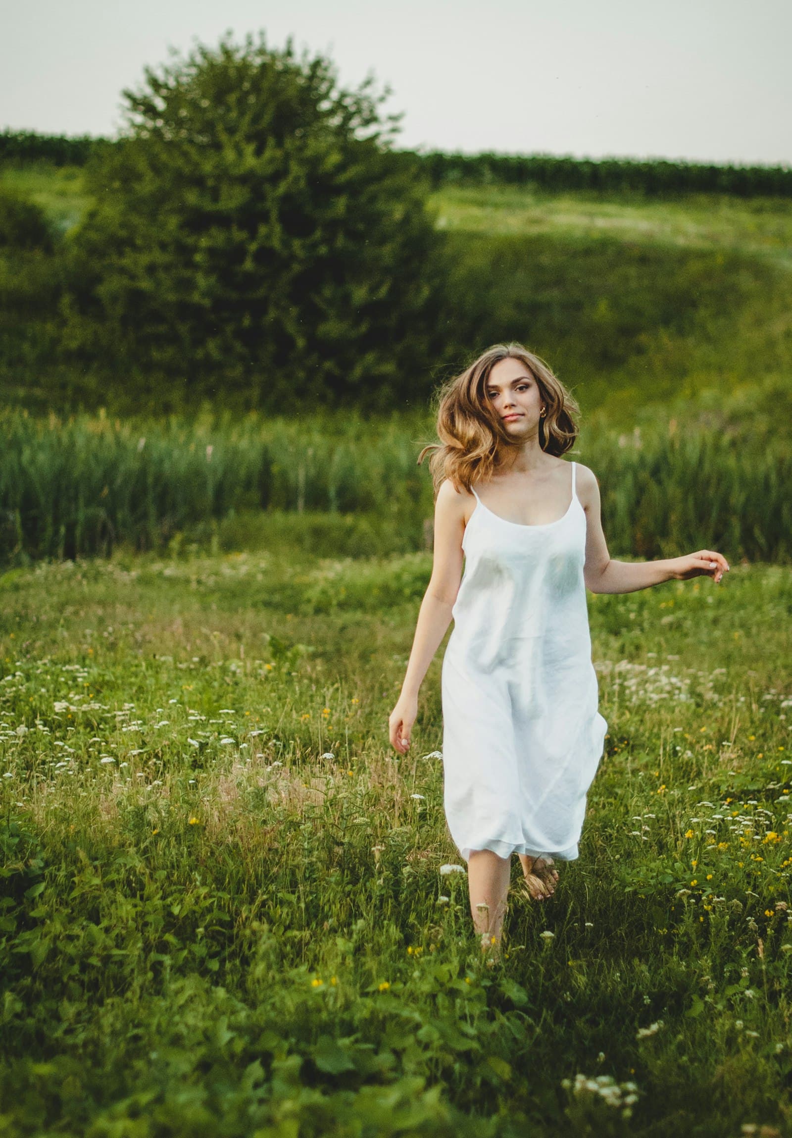 Girl in white tank dress standing on green grass field during daytime