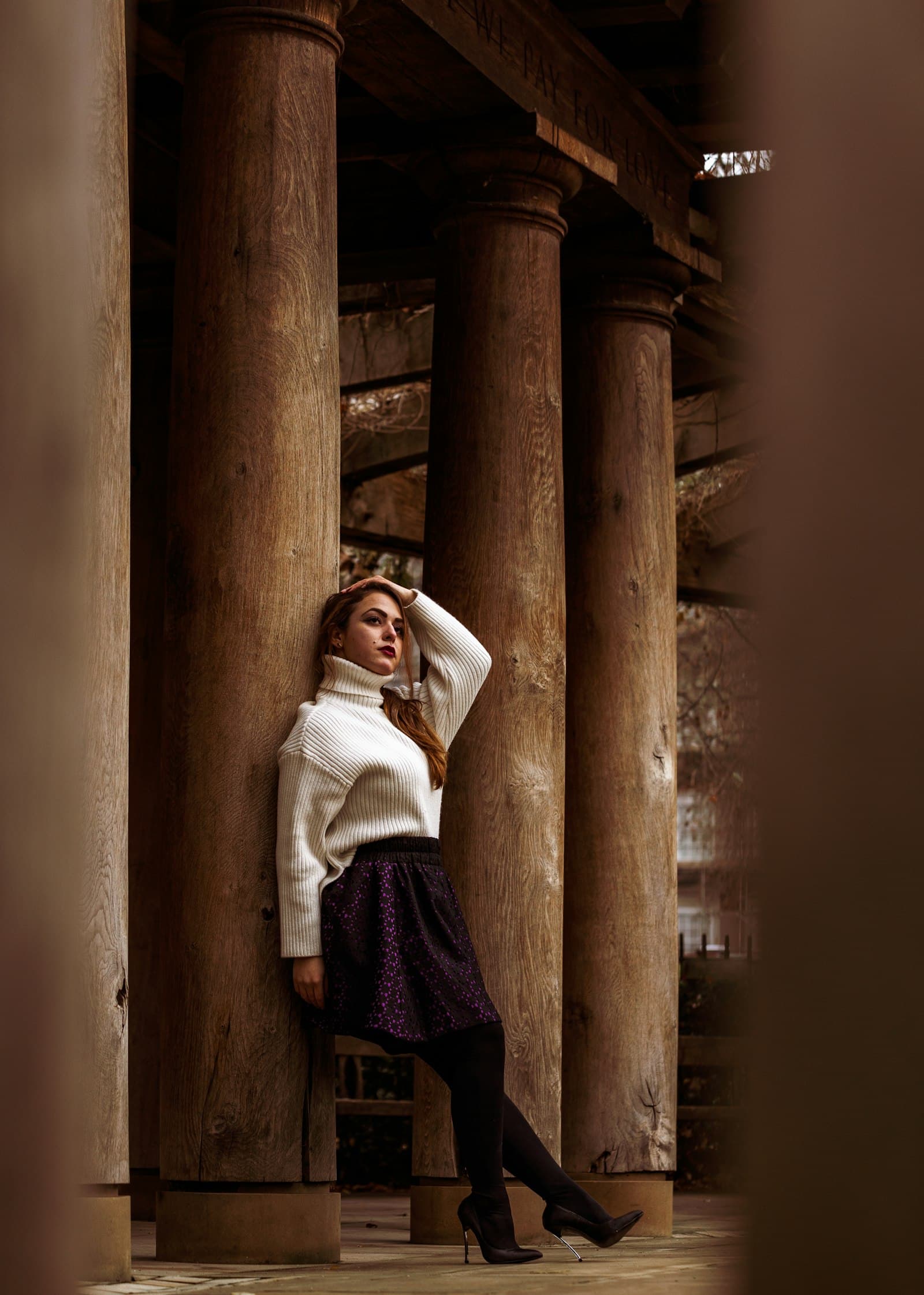 Woman in white long sleeve shirt and red skirt standing on brown concrete post